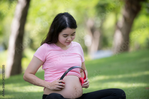 We love music, beautiful pregnant woman holding headphones on her stomach while leisurely sitting in the park with her new dad.