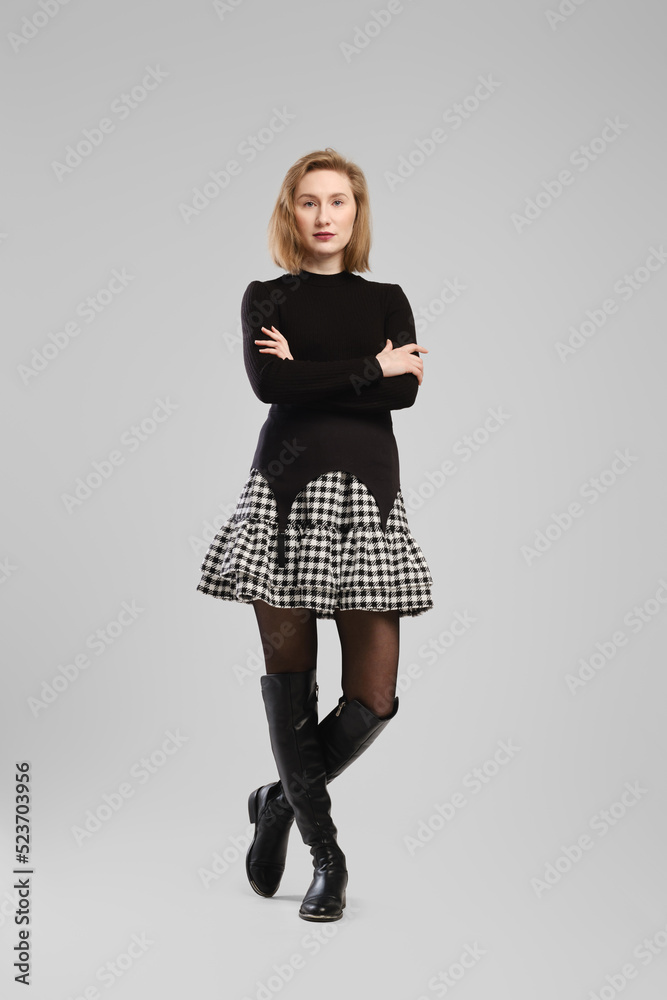 Full length portrait of young woman in turtleneck and suspender belt over little skirt posing in studio with crossed arms Full length portrait of young woman in turtleneck and suspender belt over little skirt posing in studio with crossed arms