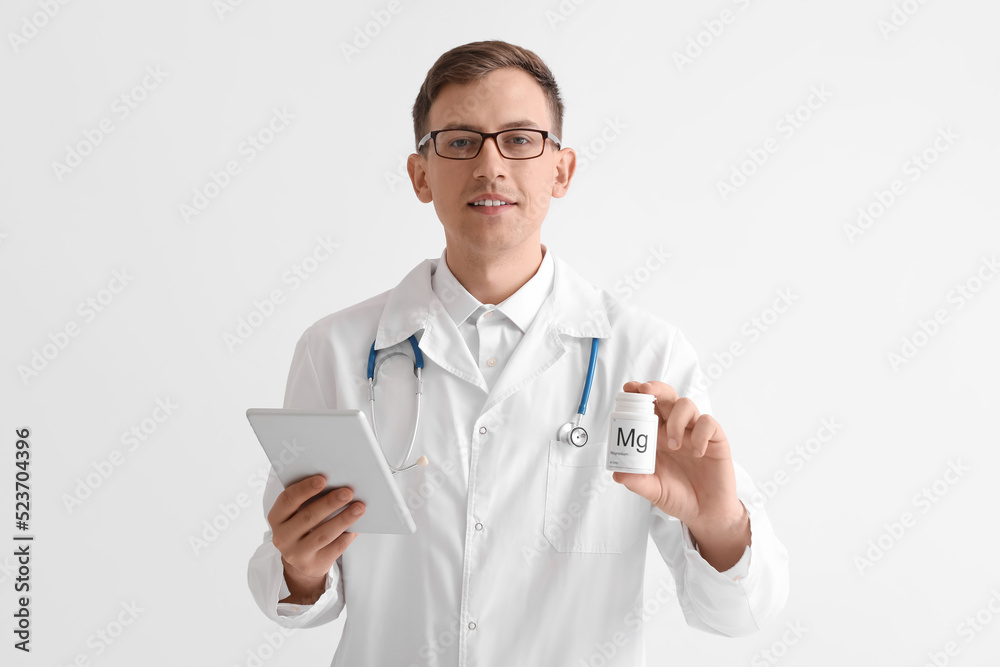 Young doctor with tablet computer and bottle of magnesium pills on white background Young doctor with tablet computer and bottle of magnesium pills on white background