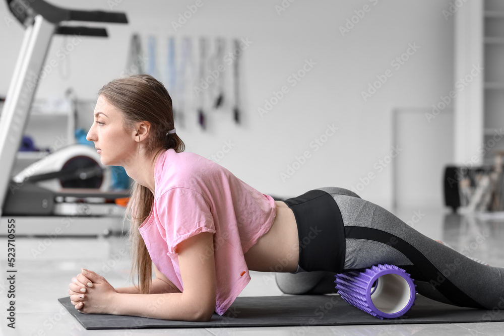 Young woman training with foam roller in gym