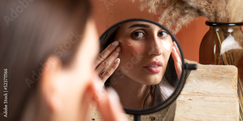 Mirror reflection of woman applying under-eye patch at dressing table closeup