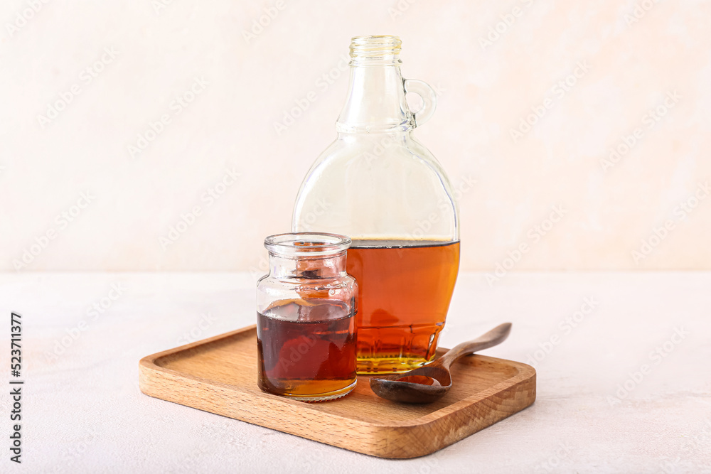 Wooden board with bottles of maple syrup on light background Wooden board with bottles of maple syrup on light background