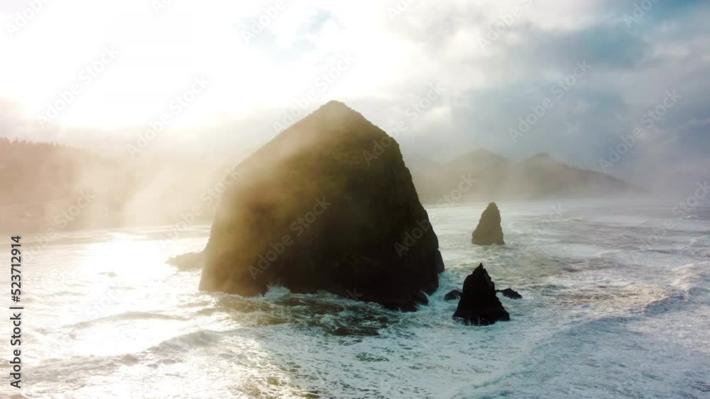 Aerial drone flying over Haystack Rock, Cannon Beach, Oregon, USA. Dramatic cloudy sunny day. Ocean waves crashing. Rocky cliff. Coastline. High quality 4k footage