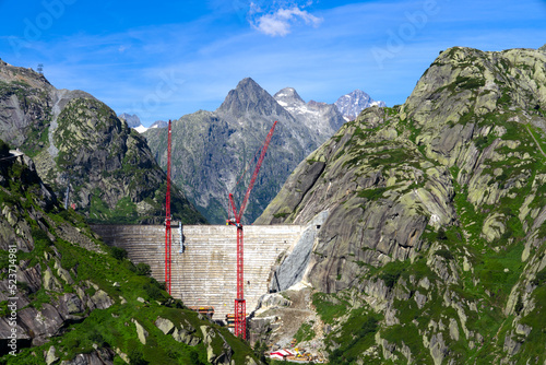 Tableau sur toile Scenic view of construction site with red cranes of new dam with lake at Swiss mountain pass Grimsel on a sunny summer day