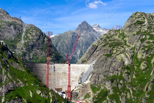 Scenic view of construction site with red cranes of new dam with lake at Swiss mountain pass Grimsel on a sunny summer day. Photo taken July 3rd, 2022, Grimsel Pass, Switzerland.