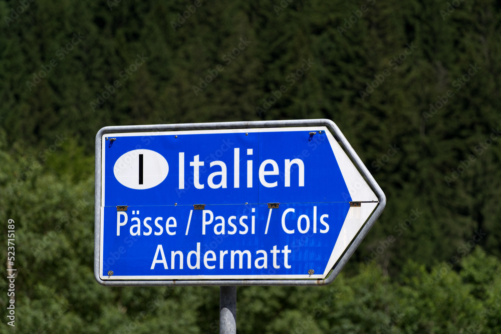 Blue direction sign to destination Italy and Andermatt at mountain village Göschenen, Canton Uri, on a sunny summer day. Photo taken July 3rd, 2022, Göschenen, Switzerland.