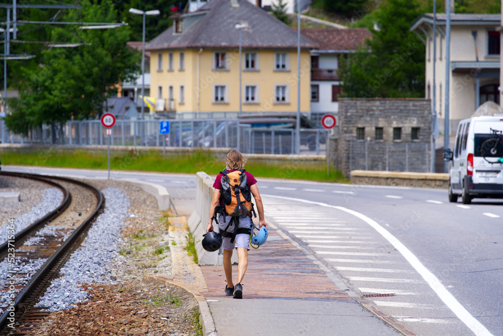 Climber on with backpack and two climbing helmets at main road of mountain village Andermatt, Canton Uri, on a sunny summer day. Photo taken July 3rd, 2022, Andermatt, Switzerland.