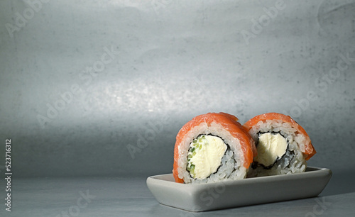 Sushi roll with philadelphia cheese and salmon on a square plate on a gray background