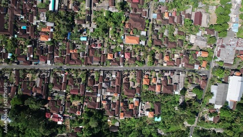 MAS village at south of Ubud town, top-down aerial panning shot. Detached buildings with tiled roofs in traditional Balinese house compounds, straight road in middle of settlement photo