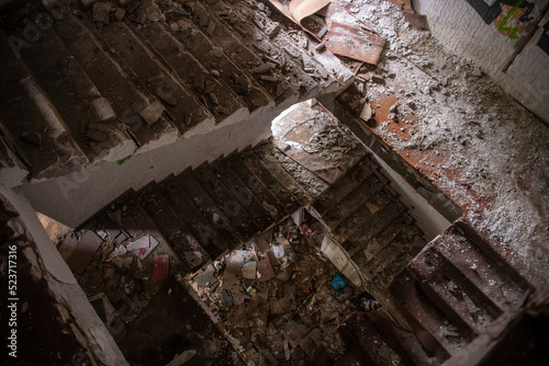 Circular staircase in Abandoned industrial building. Apocalyptic scene. Ruins of large factory covered with trash, junk, dirt and wooden furniture. Natural lighting.