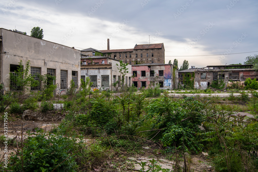 Abandoned industrial buildings. Apocalyptic scene. Ruins of large factory hangar or warehouse left behind, overgrown with vegetation.