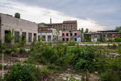 Abandoned industrial buildings. Apocalyptic scene. Ruins of large factory hangar or warehouse left behind, overgrown with vegetation. © Dragan