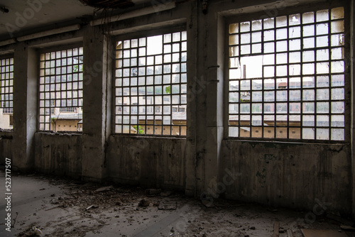 Abandoned industrial building interior. Apocalyptic scene. Ruins of large factory hangar or room covered with trash, junk, dirt and wooden furniture. Natural lighting.