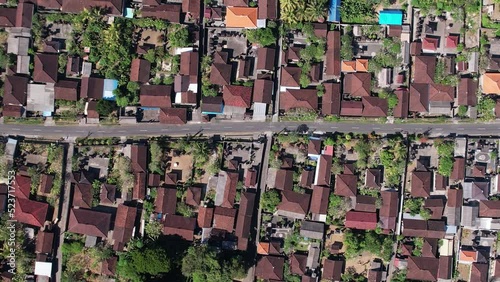 Traditional Balinese house compounds build along central road, top-down aerial shot of typical village. Camera fly up and right, looking straight down to tiled roofs of MAS village at south of Ubud photo