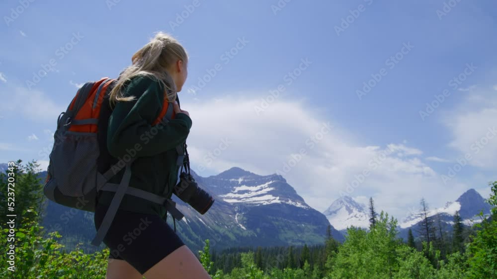 Low angle shot of mountain ranges and vast pristine ecosystem around. Close-up view of a female traveler hiking along tourist trails in Glacier National Park. High quality 4k footage Low angle shot of mountain ranges and vast pristine ecosystem around. Close-up view of a female traveler hiking along tourist trails in Glacier National Park. High quality 4k footage
