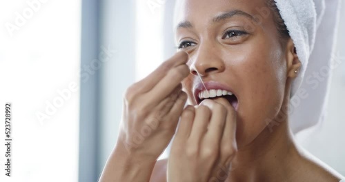 Happy, young and healthy female flossing teeth with dental floss in a bathroom looking in a mirror. Female taking care of her oral hygiene. Smiling lady doing her morning mouth routine.