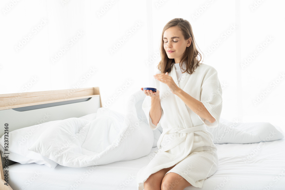 Woman caring of her beautiful skin on the face applying moisturizer on her face. Smiling girl holding little jar of skin cream and applying lotion after shower Woman caring of her beautiful skin on the face applying moisturizer on her face. Smiling girl holding little jar of skin cream and applying lotion after shower