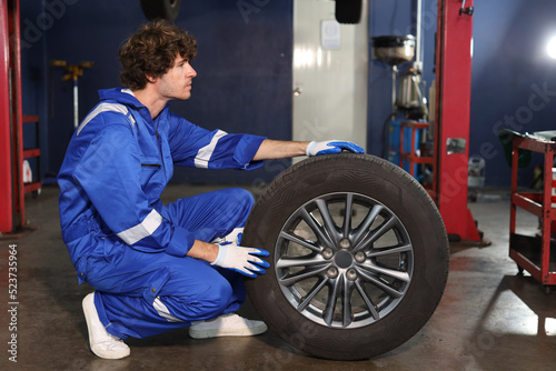 Side view portrait of man technician car mechanic in uniform holding tire for replacement or changeing at repair garage. Concept of car center repair service.