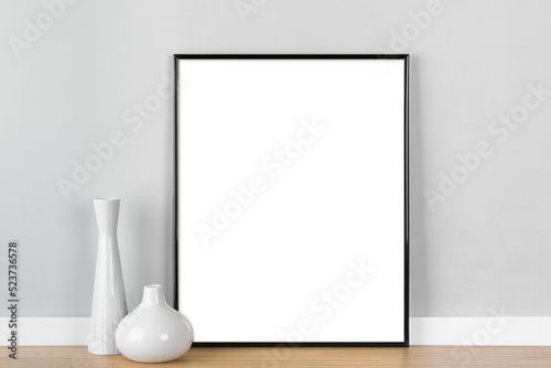 Elegant vertical black picture frame mockup, transparent template with white vases in front of  light grey wall.