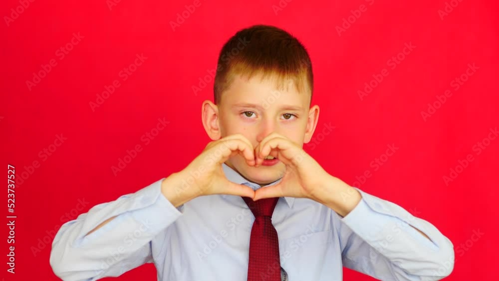 attractive caucasian boy 7-8 years old in a shirt and tie shows a heart gesture with his hands looking at the camera. studio shooting, red background. schoolboy shows a gesture of love attractive caucasian boy 7-8 years old in a shirt and tie shows a heart gesture with his hands looking at the camera. studio shooting, red background. schoolboy shows a gesture of love