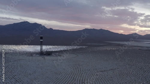 Aerial Panning Shot Of Tall Tower Amidst Solar Panels In Company By Mountains In Desert - Nipton, California photo