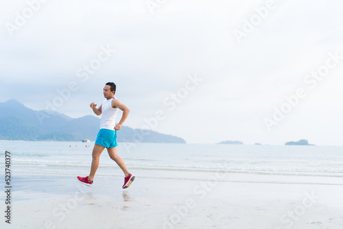 asian sport man running along seaside. running on beach with healthy toned legs body, Hamstring muscles, knee joint health active lifestyle panoramic banner background. the beach runners working out © janonkas