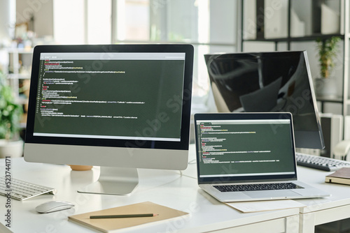 Horizontal image of computer with new software on screen with codes standing on table of programmer at office