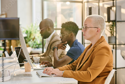 Group of programmers sitting in a row at table and working on computers at office