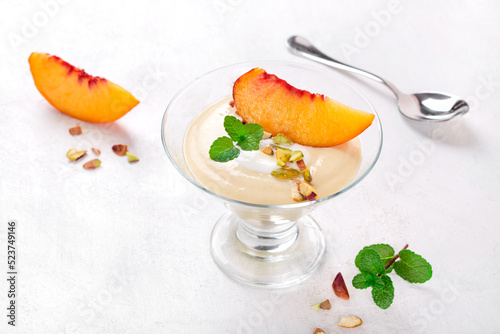 Yogurt dessert topped with nectarine slice and pistachio in glass bowl on white table