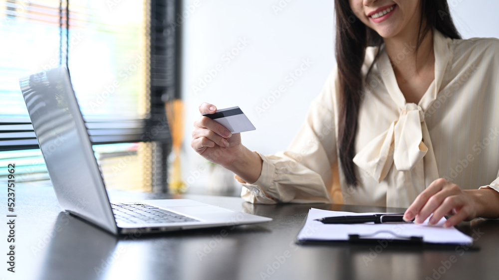 Cropped view of smiling young woman holding credit card and using laptop. Online shopping, e-commerce concept Cropped view of smiling young woman holding credit card and using laptop. Online shopping, e-commerce concept