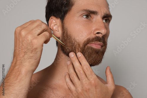 Cuadro en lienzo Man applying oil onto beard on grey background, closeup