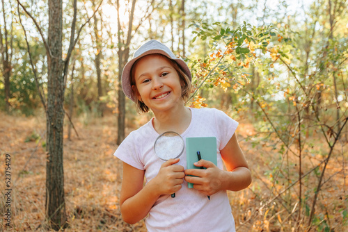 Fotografie, Obraz the portrait of a small child naturalist botanist with magnifying glass and notebook in hand, is in the forest