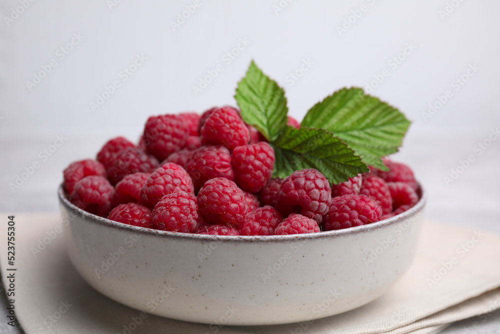 Bowl of fresh ripe raspberries with green leaves on table, closeup Bowl of fresh ripe raspberries with green leaves on table, closeup