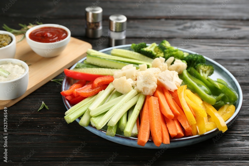 Plate with celery sticks, other vegetables and different dip sauces on dark wooden table Plate with celery sticks, other vegetables and different dip sauces on dark wooden table
