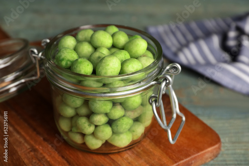 Tasty wasabi coated peanuts in glass jar on wooden table, closeup