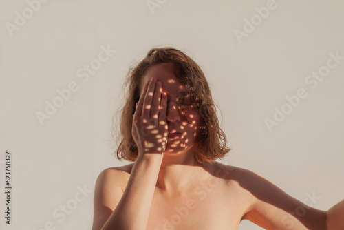 Ashamed girl covering half of face because of zits presented by light. Woman suffering from pimples and hiding them. Psychological problems due to stains, spots on skin. Acne during puberty concept.