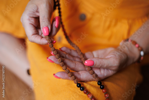 Closeup of woman hands sorting out brown beads. Beautiful rose nails. Hands with manicure. Yellow dress background. Person meditating and praying
