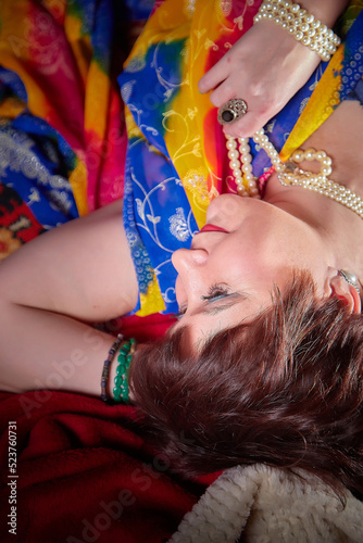 A beautiful European girl with short hair looking like an Arab woman in a red room in a harem. Photo shoot of an oriental style odalisque. A model poses in a sari