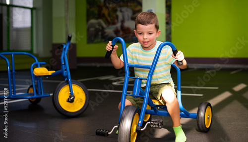 A six-year-old child boy rides a blue tricycle on a special area with markings on the road photo