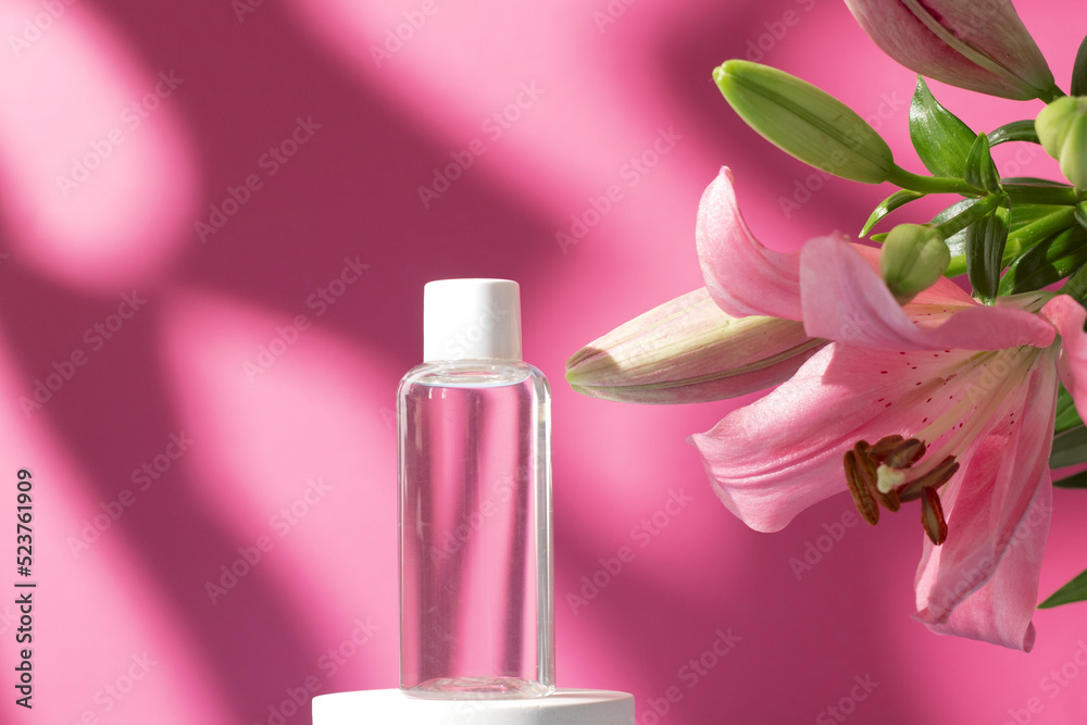Cosmetic bottle with tonic water on podium with lily flower and shadow on pink background. Face and body care spa concept. Hyaluronic acid oil, serum with collagen and peptides skin care product Cosmetic bottle with tonic water on podium with lily flower and shadow on pink background. Face and body care spa concept. Hyaluronic acid oil, serum with collagen and peptides skin care product