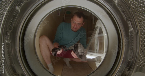 A man throws laundry into the washing machine. He throws objects into the drum of the washing machine. Closes the glass hatch with his hand. CZ, Kladno, Polska, 25.5.22 photo