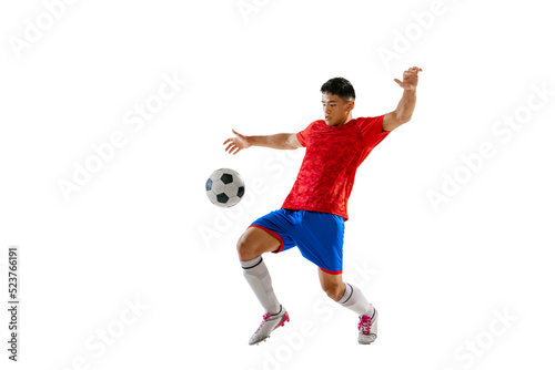 Portrait of young man, football player training, playing, kicking ball isolated over white studio background