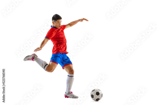 Portrait of young man, professional football player in motion, training, dribbling ball isolated over white studio background