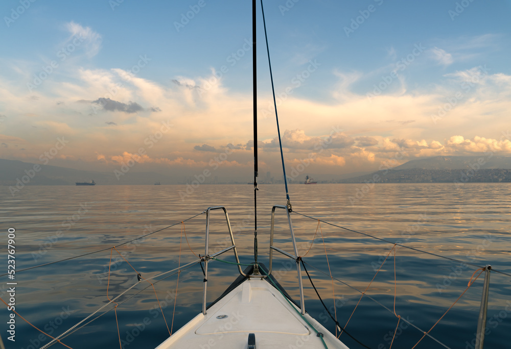 Yacht sailing at the sunset with cloudy sky, nose view.