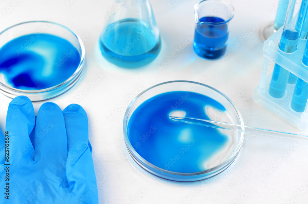 Antiviral vaccine development. Laboratory glassware with blue and cyan liquid on a white table. Scientific laboratory research Antiviral vaccine development. Laboratory glassware with blue and cyan liquid on a white table. Scientific laboratory research