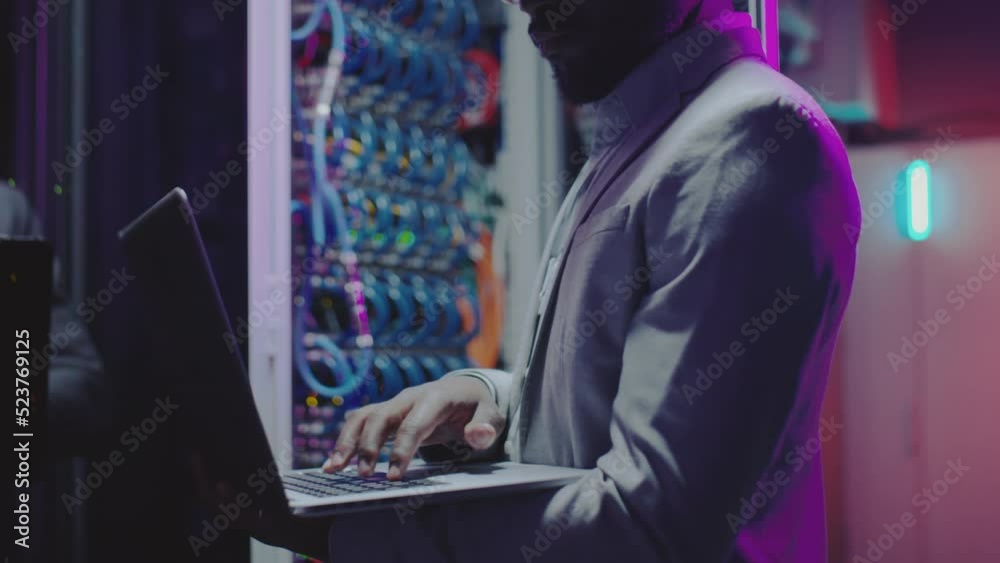 Cropped shot of African American data center engineer using laptop while working in server room