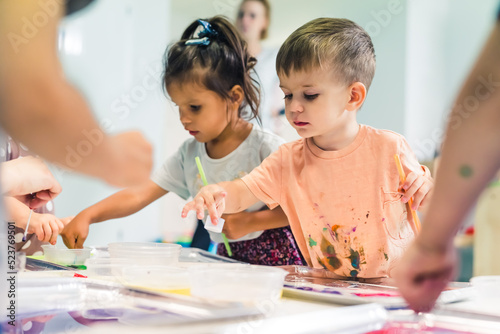 Multi-ethnic group of toddlers milk painting with the teacher helping them, using nontoxic paint, food coloring for colors. Children finger painting at the nursery school class. High quality photo