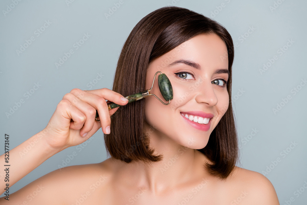 Fototapeta premium Portrait of joyful smile lady apply jade gua sha beauty tool massage silky soft pure skin treatment isolated over grey color background