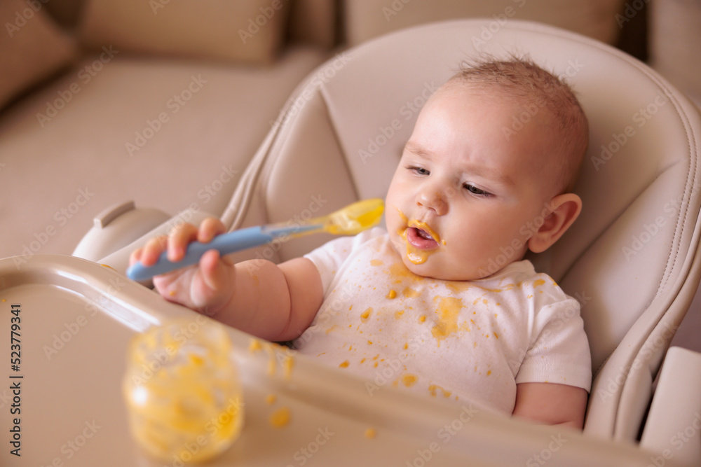 Cheerful funny baby boy sitting in high chair, holding spoon and playing Cheerful funny baby boy sitting in high chair, holding spoon and playing