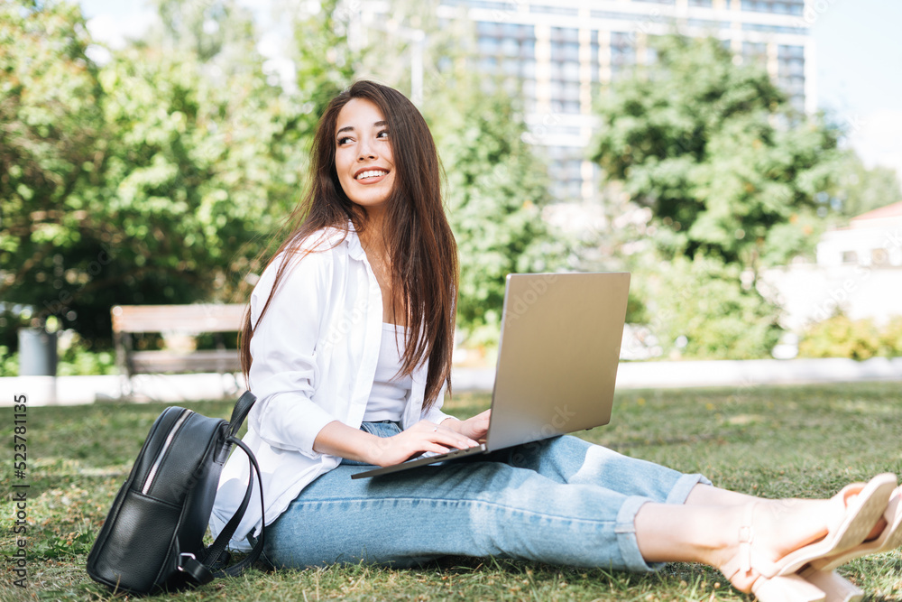 Young asian woman student freelancer with long hair working on laptop in city park Young asian woman student freelancer with long hair working on laptop in city park